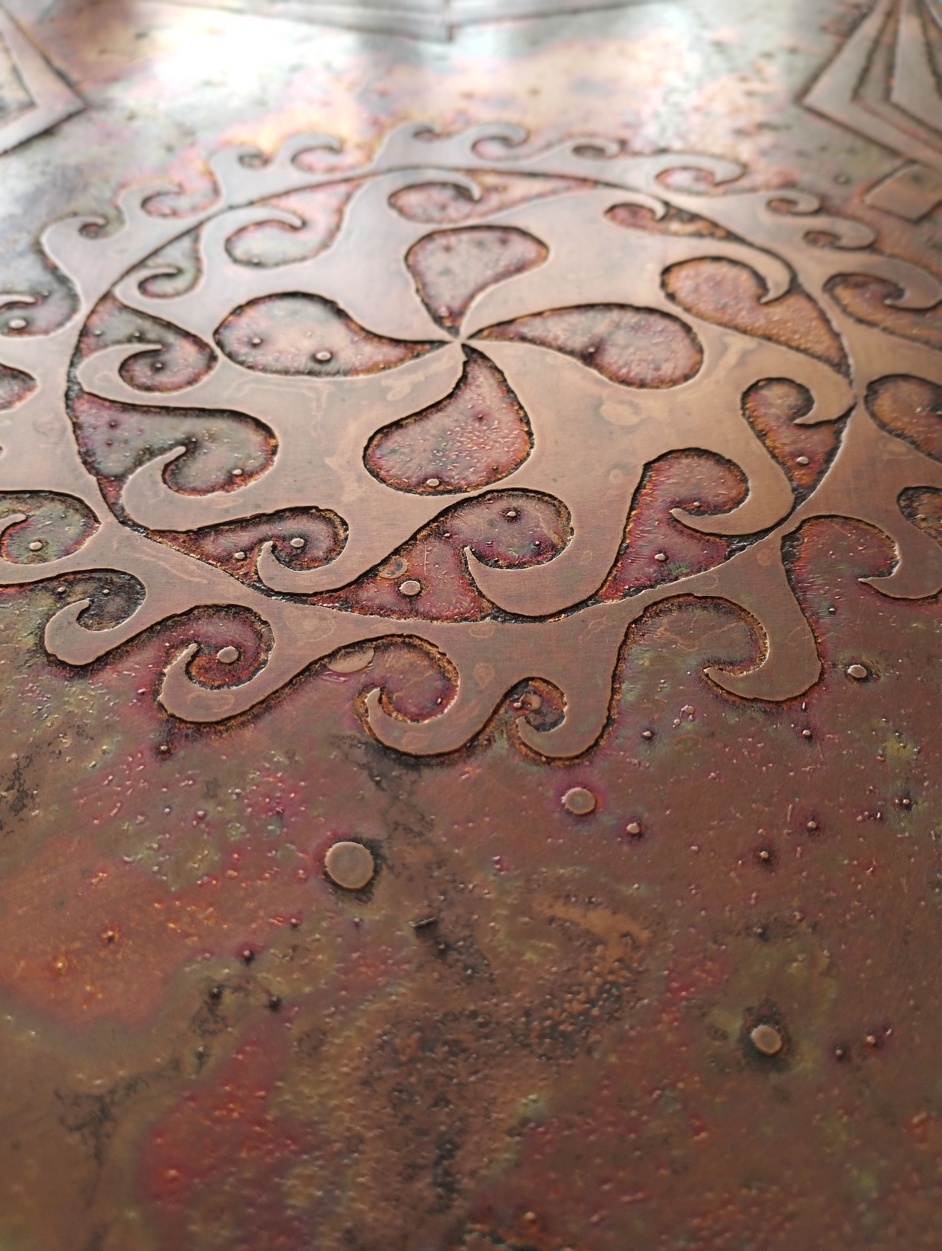 gravure sur cuivre Le motif est croix basque encerclée d'un motif de vagues. La Patine de finition est naturelle et brulée. La texture du cuivre ressort avec des effets rouge et orange parfois brun.