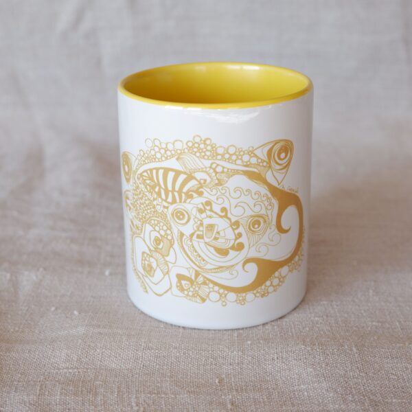 Cette photo est un gros plan sur le Mug en céramique avec anse, intérieur jaune acidulé et motif d'artiste jaune ocre où se mêlent poissons, vagues, bulles, fleurs et feuilles. Il est photographié sur un étoffe en lin naturel.