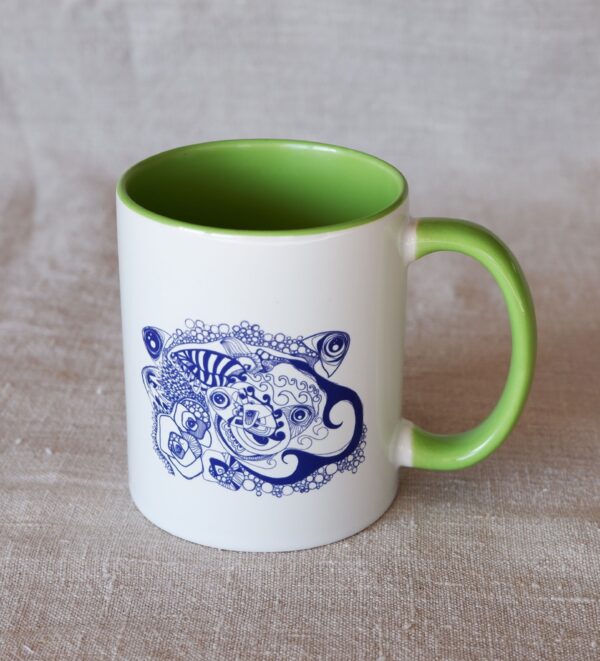 Un Mug en céramique blanche avec une anse et l'intérieur vert uni franc où est imprimé un dessin d'artiste bleu marine où se mêlent poissons, vagues, bulles, fleurs et feuilles. Il est photographié sur un tissu en lin naturel.