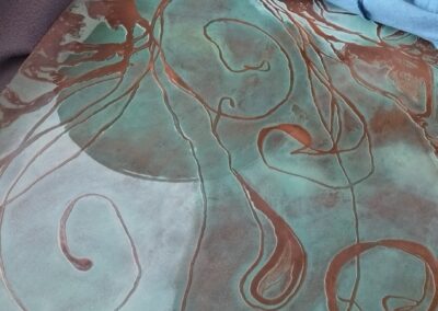 Application de cire tiède sur une gravure en cuivre patiné pour protéger la surface et révéler les reliefs.