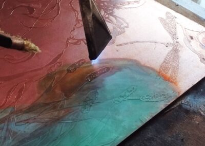 Application au pinceau de la patine Vert Empire chauffée au chalumeau sur une plaque de cuivre gravée pour un projet de mobilier d'art.