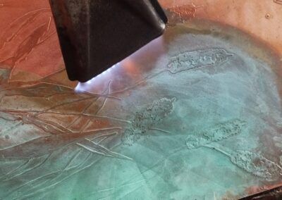 Application de la patine Vert Empire au chalumeau éventail sur une plaque de cuivre gravée.