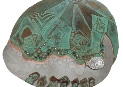 Œuvre murale contemporaine en cuivre patiné, gravée et émaillée, représentant un paysage imaginaire avec un village, une rivière et un poisson, réalisée par Muriel Carcagno au Pays Basque.