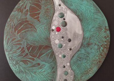 Tableau mural rond en cuivre gravé, repoussé et patiné, associé à l'aluminium et orné d'un cabochon rouges émaillé, création de Muriel Carcagno.